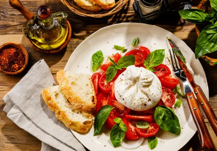 Pyszna burrata, czyli straciatella ser, z pomidorami i bazylią, podana z chrupiącym pieczywem i oliwą.