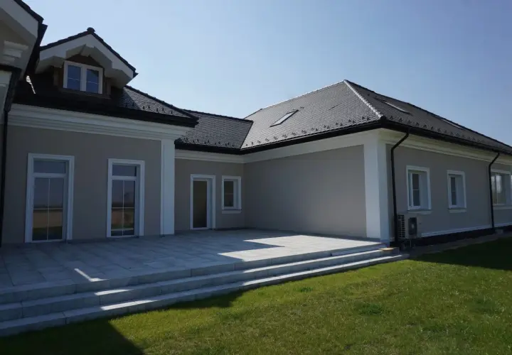 Elegancki dom z tarasem i trawnikiem. Biały gzyms podkreśla architekturę budynku.
