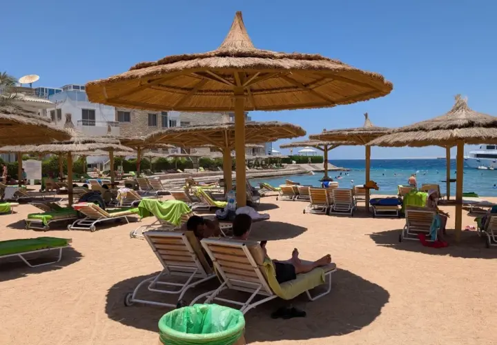 Egipt last minute all inclusive najtaniej: piaszczysta plaża z leżakami i parasolami, turkusowe morze, hotel w tle. Idealne miejsce na relaks.