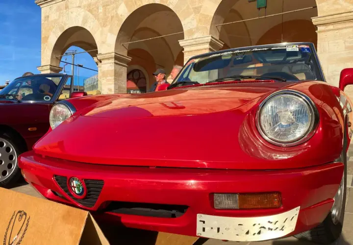Dreaming of renting a car in Italy? This classic red Alfa Romeo convertible, parked under arched buildings, evokes the perfect Italian road trip.
