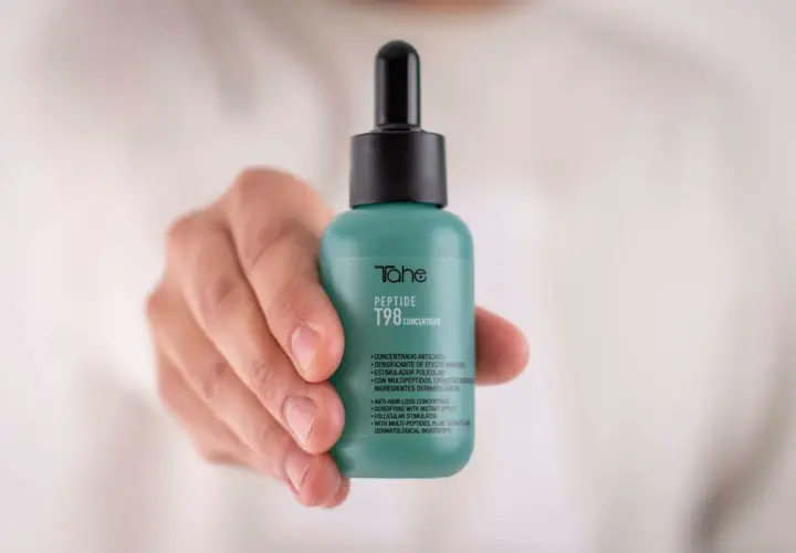 Mano sostiene frasco verde con peptidos para el pelo, concentrado anticaída T98 de Tahe.