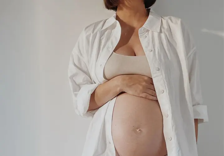 Przyszła mama w białej koszuli czule trzyma brzuch. Zastanawia się nad depilacją laserową w ciąży.