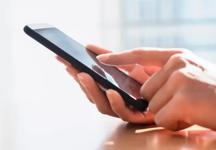 Dłoń dotyka ekranu smartfona, szukając archiwum SMS.