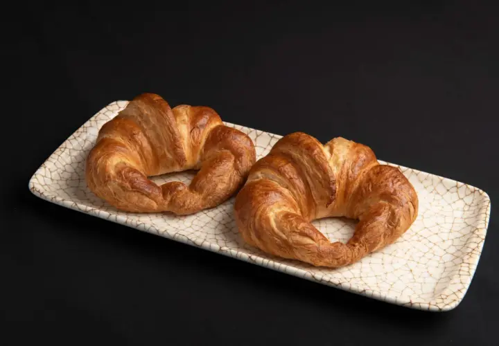 Dos croissants dorados, listos para disfrutar. El hojaldre crujiente invita a hacer croissant con hojaldre casero.