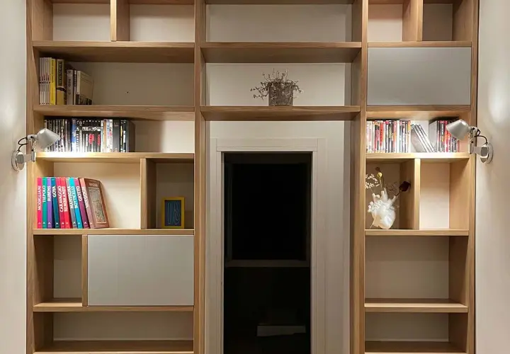 Parete in legno fai da te con libri, DVD e decorazioni. Illuminazione discreta valorizza gli oggetti.