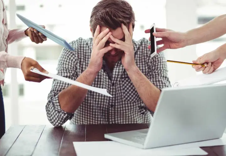 Uomo stressato, sommerso da richieste: tablet, fogli, telefono, matita. Il superlativo di busy è qui.