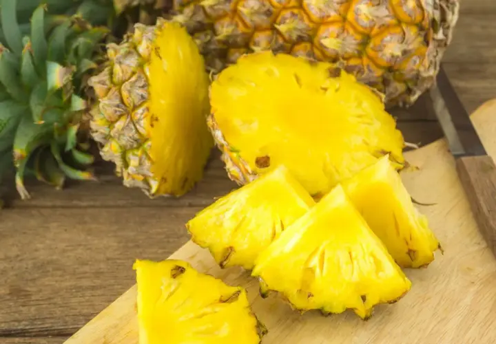Soczyste kawałki ananasa na desce, obok całego owocu. Czy ananas jest zdrowy? Tak, to bomba witaminowa!