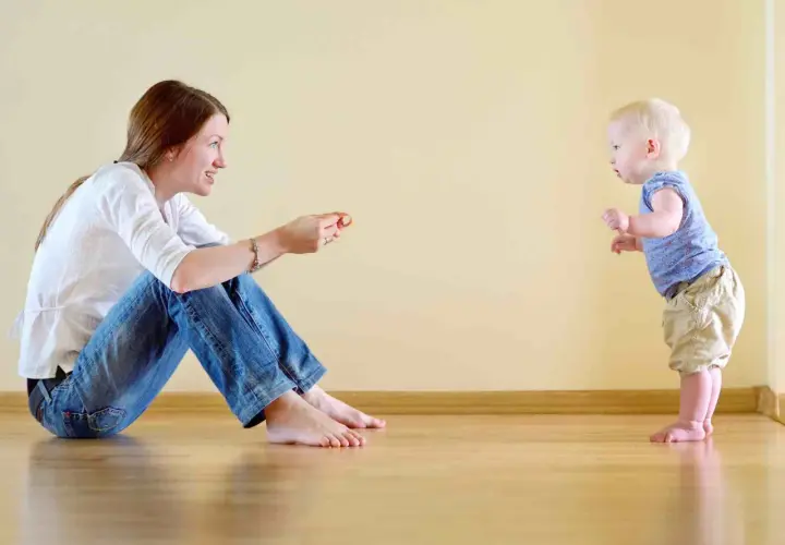 Mamma incoraggia il suo bambino, che sta imparando quando iniziano a camminare i bambini, a fare i suoi primi passi.