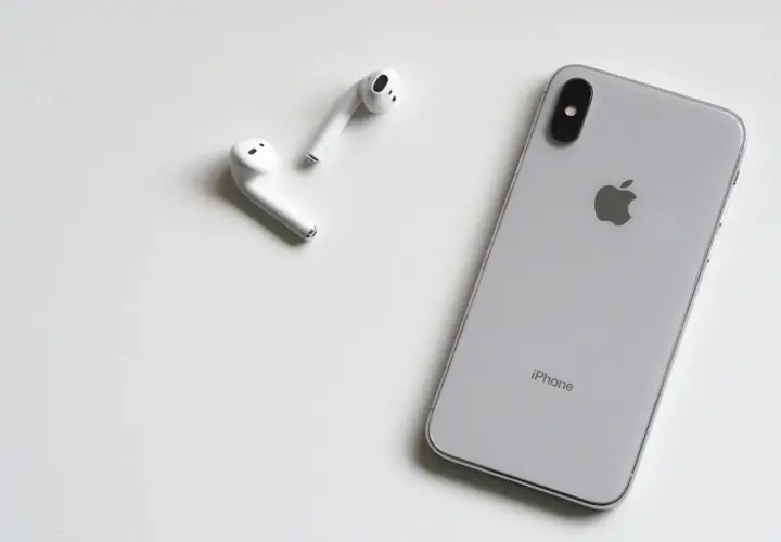 Srebrny iPhone i białe słuchawki AirPods leżą na białym tle. Może rozmówca na iPhonie słabo słychać?