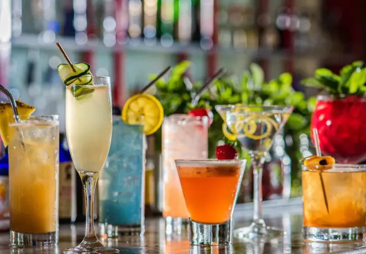 En rad färgglada drinkar, inklusive en sockerlag drink med gurka, står uppradade på en bardisk.