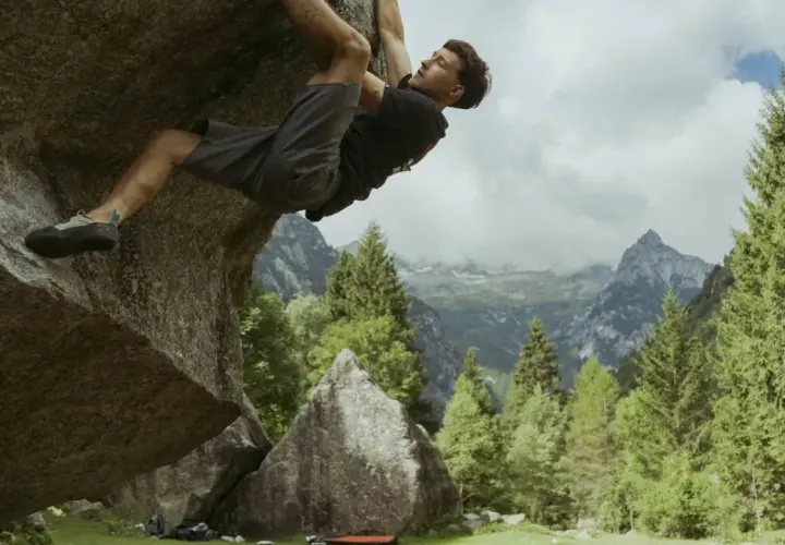Mężczyzna wspina się po skale w górach, stosując zasady boulderingu. W tle piękne krajobrazy.
