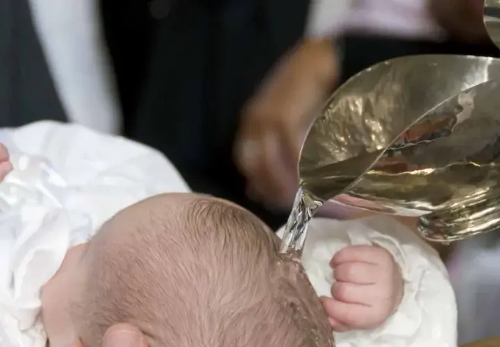 Taufe eines Babys mit Wasser aus einem silbernen Gefäß.