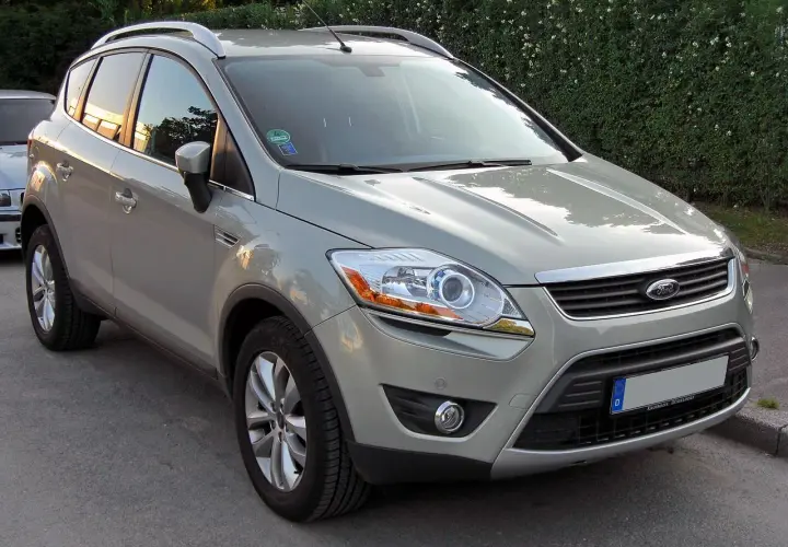 Szary Ford Kuga, SUV, prezentuje swoje wymiary na tle zielonego żywopłotu.