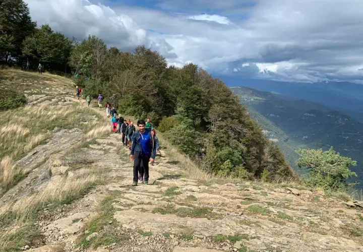 Grupo de excursionistas recorre la ruta puigsacalm, un sendero rocoso con vistas a un valle boscoso bajo un cielo nublado.