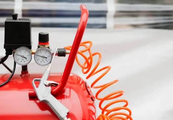 Detalles de un compresor de aire rojo con manómetros y pistola. Aprende como limpiar un compresor de aire para un óptimo funcionamiento.