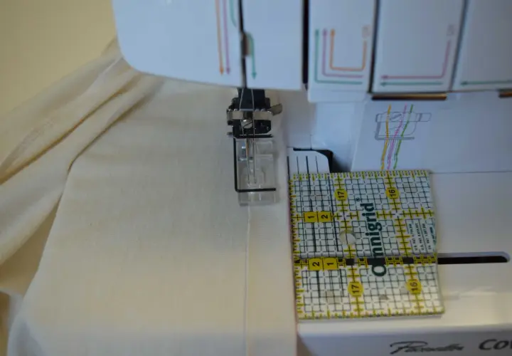 A ruler guides fabric under a coverstitch machine needle, showing how to use a coverstitch machine for precise hemming.