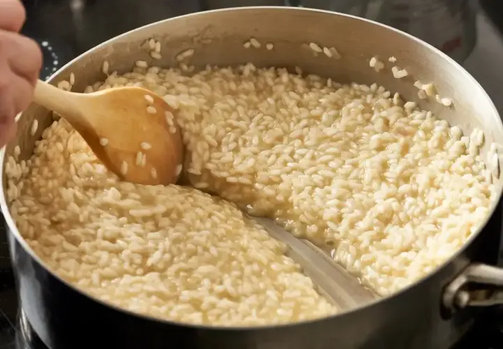 Drewniana łyżka miesza kremowy ryż do risotto w garnku.