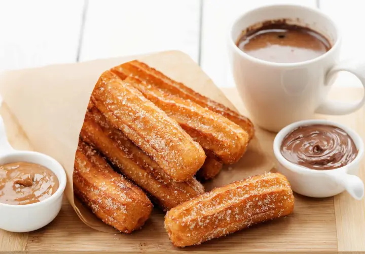 Churros dorés et croustillants, saupoudrés de sucre, prêts à être trempés dans le chocolat. Une recette gourmande pour un goûter parfait.