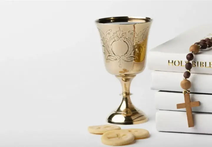 Złoty kielich, stos białych ksiąg z napisem "HOLY BIBLE", różaniec i opłatki. Symbolika sakramentu, który może być odnotowany w akcie chrztu.