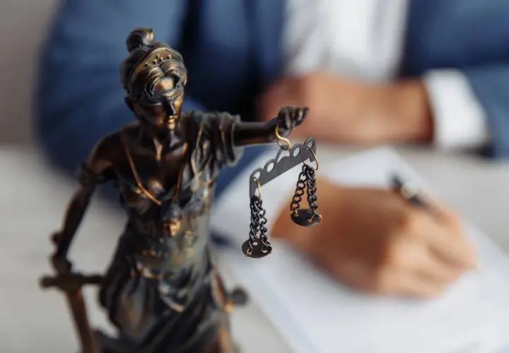 Figurka Temidy z wagą symbolizuje sprawiedliwość. W tle prawnik sporządza dokumenty dotyczące uchylenia postanowienia o stwierdzeniu nabycia spadku.