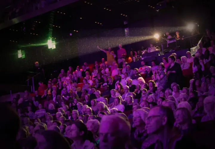 Publik njuter av en konsert i Uppsala. Scenen badar i lila ljus, och en artist gestikulerar mot publiken.