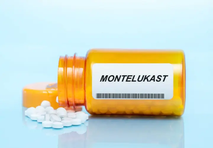 Pomarańczowa buteleczka z lekami na astmę, z etykietą "MONTELUKAST" i rozsypanymi tabletkami.