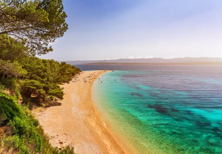 Traumhafter kroatischer Strand mit Pinienwald und türkisfarbenem Wasser. Menschen entspannen sich am Zlatni Rat Strand.