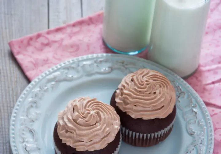 Deux cupcakes au chocolat avec une ganache chocolat passion onctueuse, servis sur une assiette bleue avec deux verres de lait.