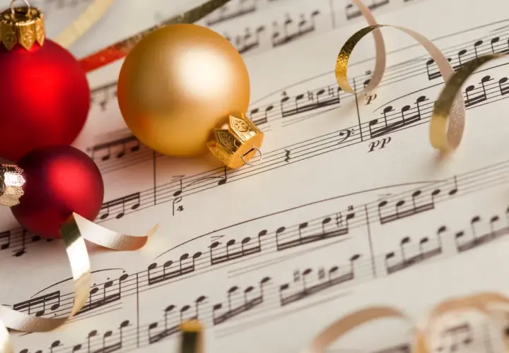 Palline rosse e dorate su spartito musicale, un'anticipazione delle 10 canzoni di Natale più popolari.
