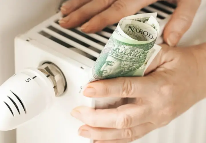Ręce trzymają banknot 100 zł przy grzejniku. Sprawdzanie rachunków za ogrzewanie, cennik pogotowia gazowego.