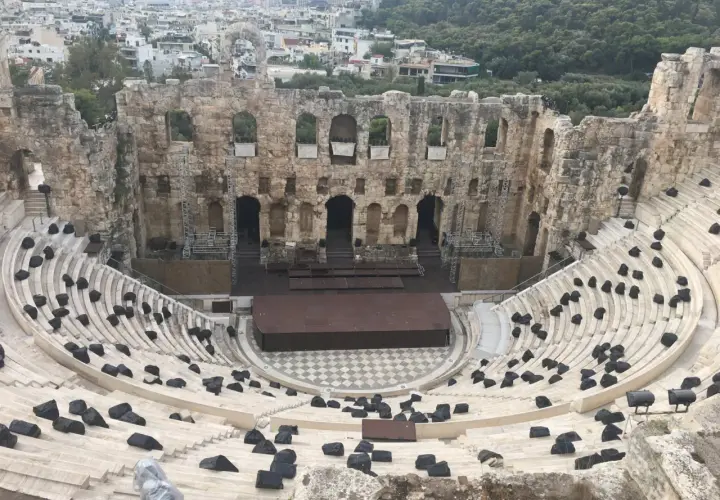 Starożytny Odeon Heroda Attyka w Atenach, z kamiennymi siedzeniami i sceną, w tle widać miasto.