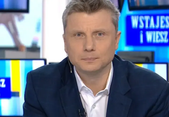Rafał Wojda, wiek dziennikarza widoczny w jego spojrzeniu, w garniturze przed ekranem z napisem "Wstajesz i wiesz".
