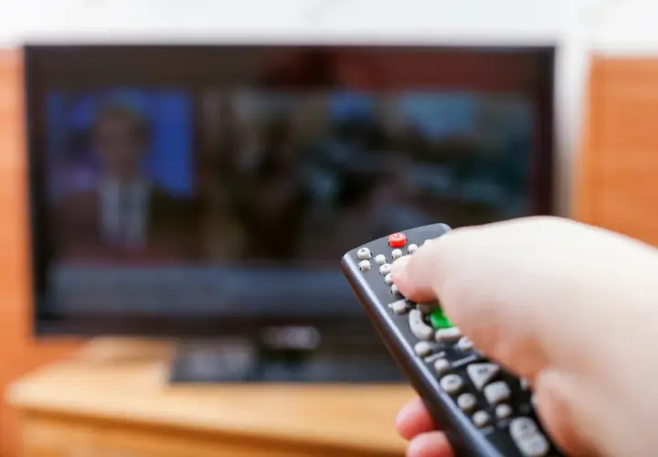 Dłoń z pilotem przed telewizorem, być może to już koniec abonamentu rtv i czas na zmiany.