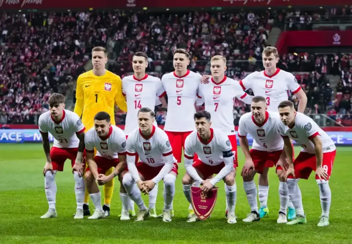 Piłkarze reprezentacji Polski w białych strojach pozują na murawie stadionu.