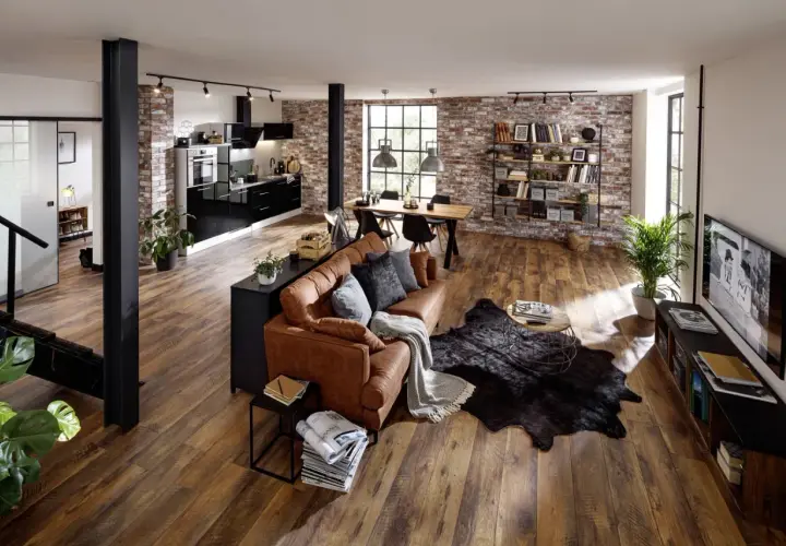 Gemütliches **vintage industrial style wohnzimmer** mit Ledersofa, Holzboden und Ziegelwand. Offene Küche und Essbereich im Hintergrund.