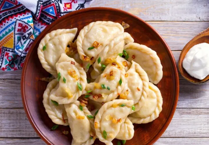 Pyszne pierogi z bryndzą, posypane skwarkami i szczypiorkiem, podane z łyżką śmietany.