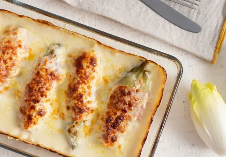 Endivias a la plancha con jamón, gratinadas con queso y bechamel en una fuente de cristal.