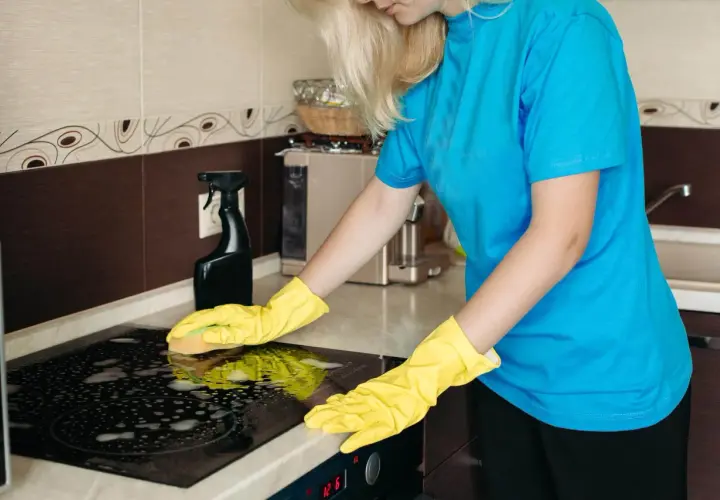 Mujer con guantes amarillos limpiando la placa de inducción con espuma.