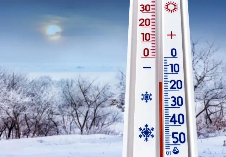 Termometr pokazuje -10°C, co zapowiada mroźną pogodę na styczeń 2026. Zimowy krajobraz z ośnieżonymi drzewami i bladym słońcem.