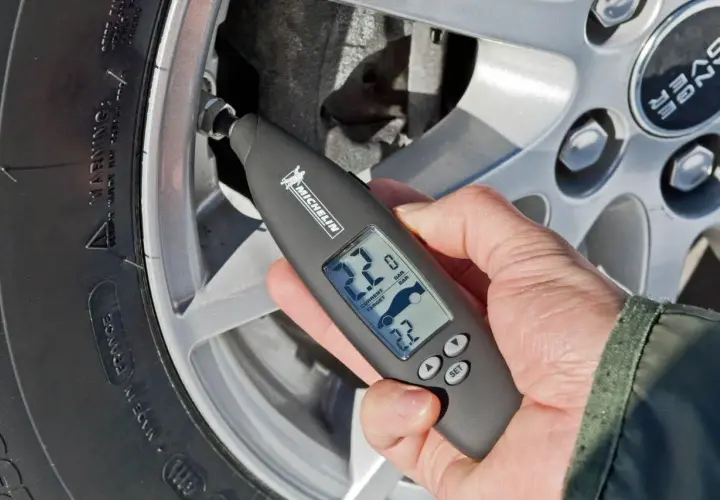 Mano usa un medidor digital Michelin para comprobar la **pegatina presión neumáticos** de un coche.