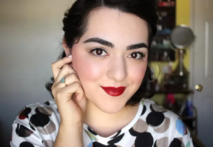 Mujer con un look de maquillaje años 40, labios rojos intensos, delineado de ojos y rubor rosado.