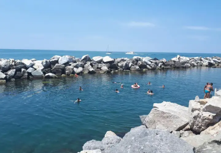 Baignade estivale dans la marina de Pise, avec des rochers formant une digue et des baigneurs profitant du soleil.