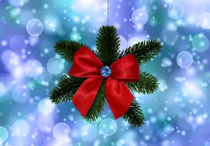 Un lazo de navidad rojo brillante adorna una rama de pino, suspendido sobre un fondo azul con luces bokeh.