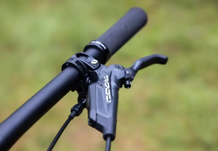 Close-up of a bicycle handlebar with a black brake lever. The lever has "KOO" branding, suggesting a brake fluid comparison.