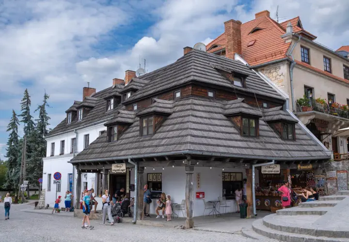 Tętniący życiem rynek w Kazimierzu Dolnym. Ludzie spacerują, kupują lody i gofry, podziwiając zabytkową architekturę.