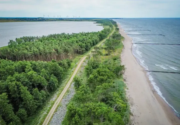 Malownicza nadmorska trasa rowerowa biegnie wzdłuż lasu i plaży, z widokiem na morze i jezioro.