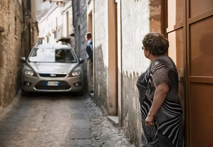 Navigating narrow Italian streets: a silver car is parked in a tight alleyway. Tips for driving in Italy for the first time include being prepared for tight squeezes.