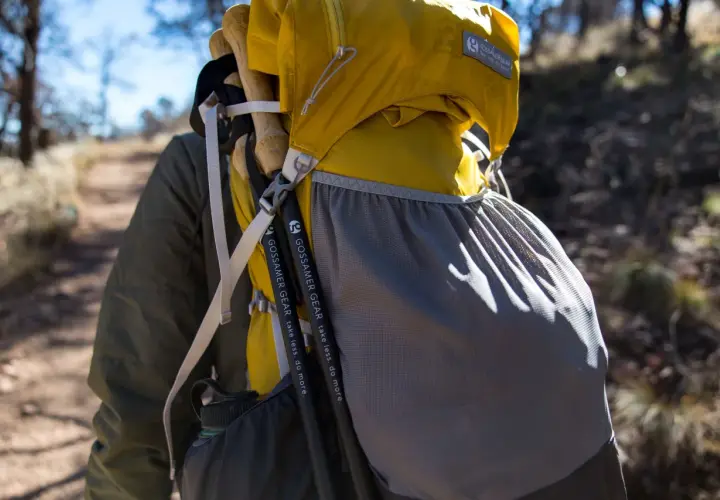 Kijki trekkingowe przymocowane do żółtego plecaka Gossamer Gear. Paski i siatkowa kieszeń pomagają w transporcie.