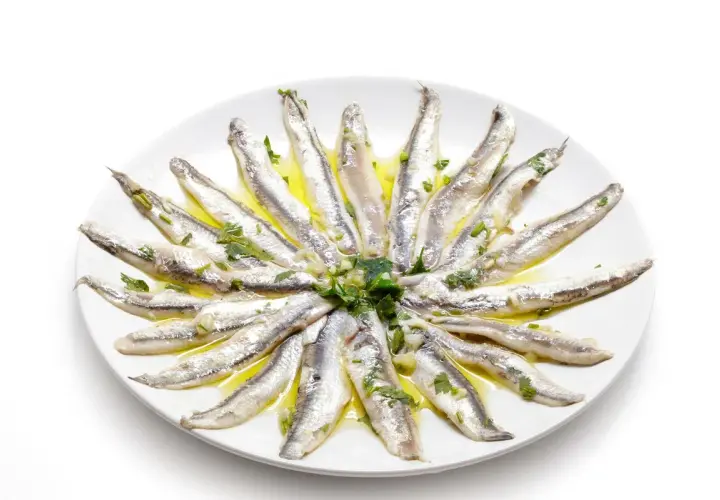 Acciughe al verde disposte a raggiera su un piatto bianco, condite con olio, aglio e prezzemolo.