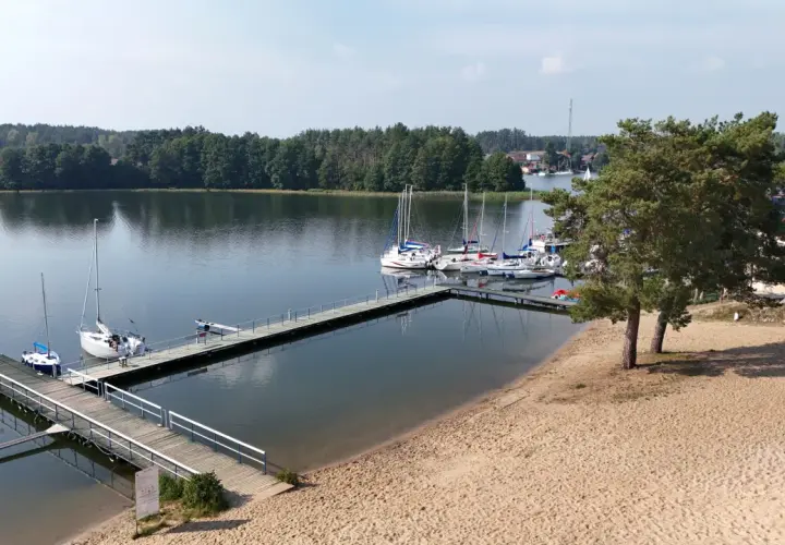 Słoneczna plaża nad jeziorem Wdzydze, z pomostami i żaglówkami. Idealne miejsce na wypoczynek.